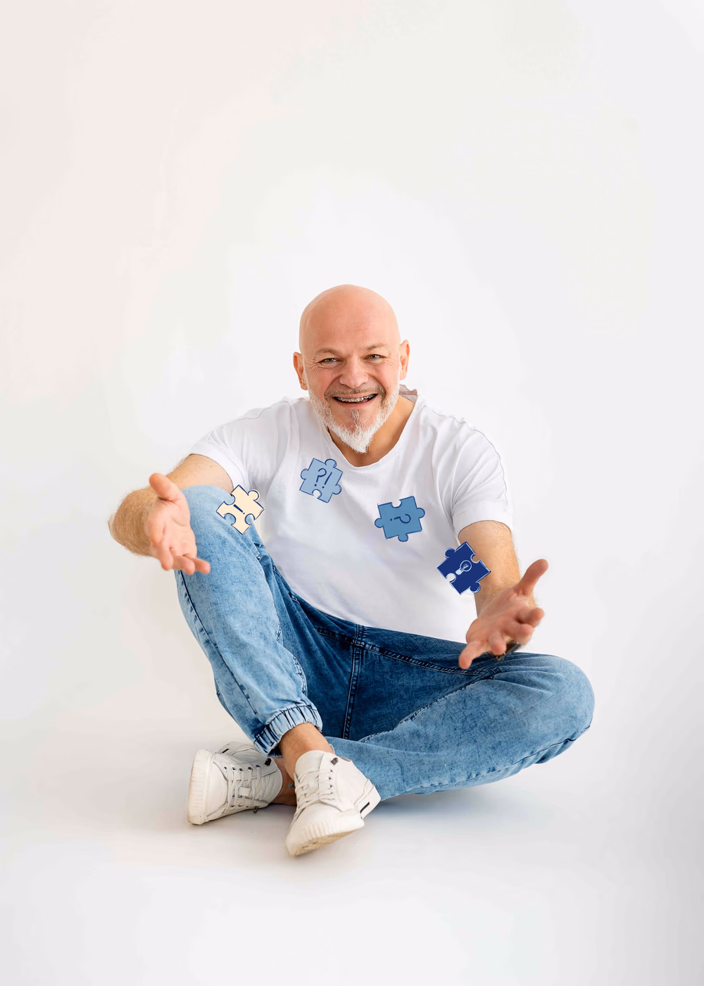 Wojciech Męciński siedzi po turecku i wyciąga obie dłonie w stronę patrzącego, wokół niego cztery puzzle